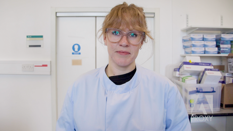 Edel smiling in her lab coat, whilst standing in a lab.