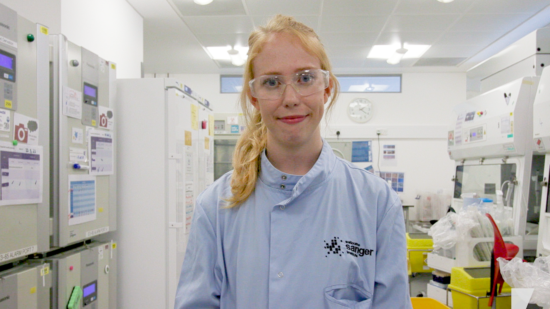 Picture of Lucy smiling, she is in a lab coat and protective glasses in the lab.