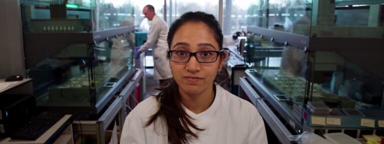 Picture of Niki smiling surrounded by a lab with scientists working behind her.