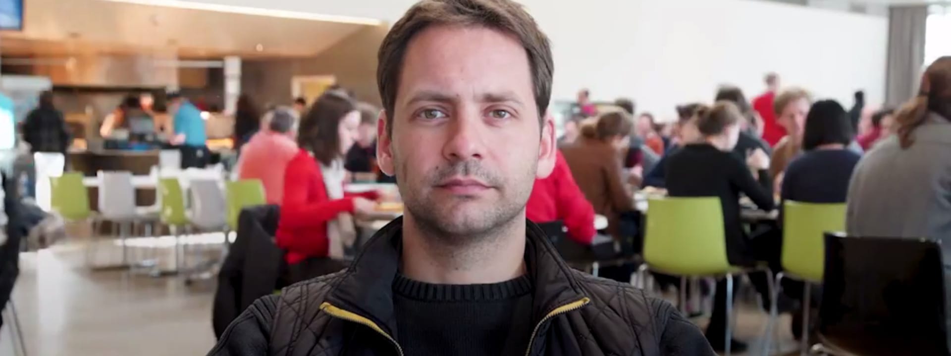 Picture of Roland, he is sitting in the cafeteria with multiple people in the background.