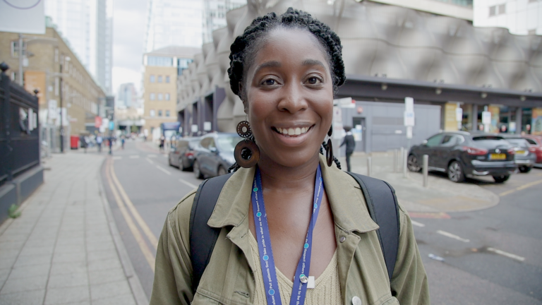 Picture of Sasha smiling happily. Sasha is outside in a built up city standing beside a road.