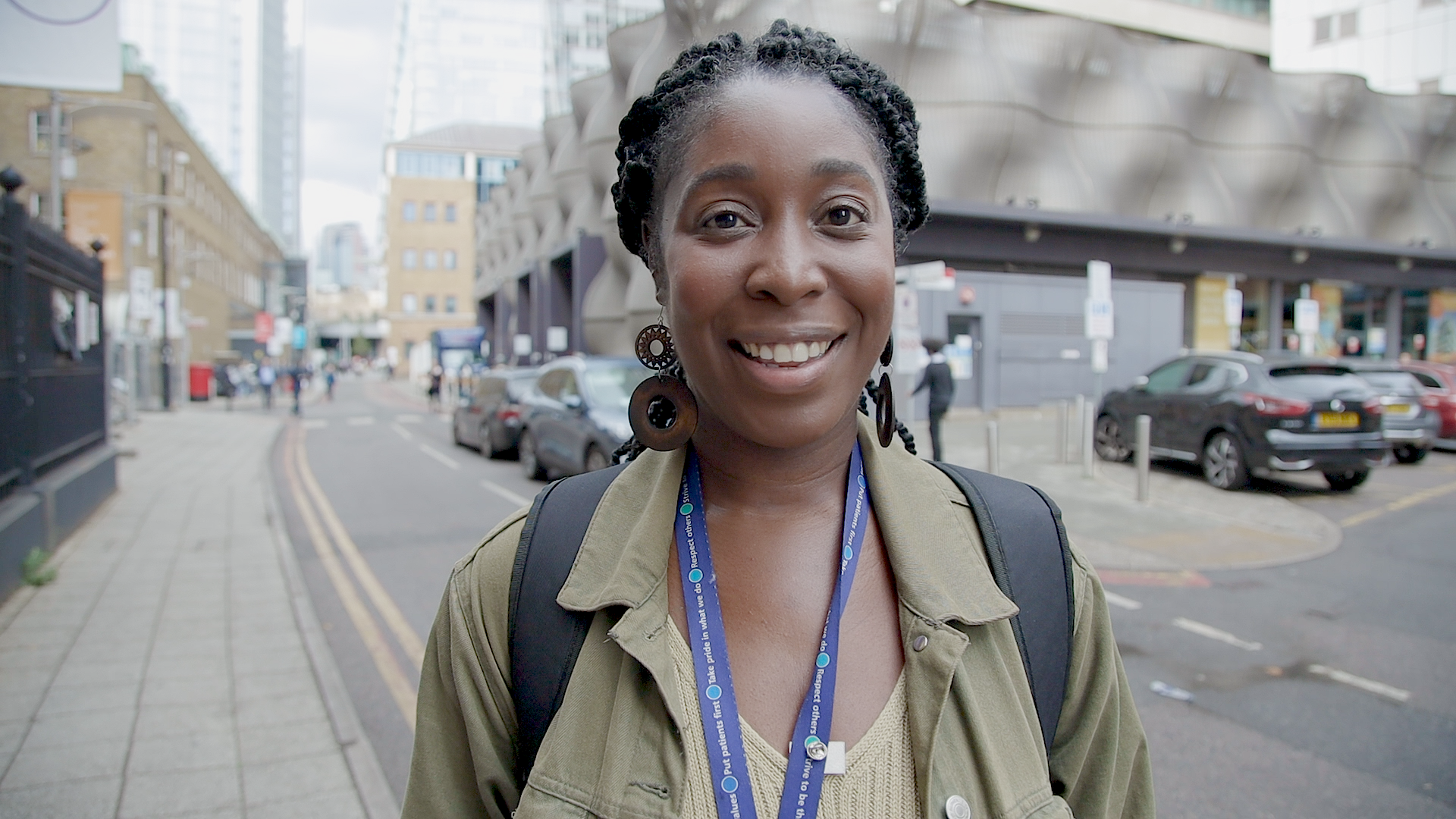 Picture of Sasha smiling happily. Sasha is outside in a built up city standing beside a road.