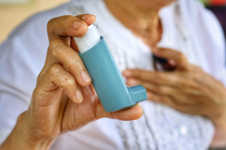 Elderly female hand using an inhaler while having difficulty breathing