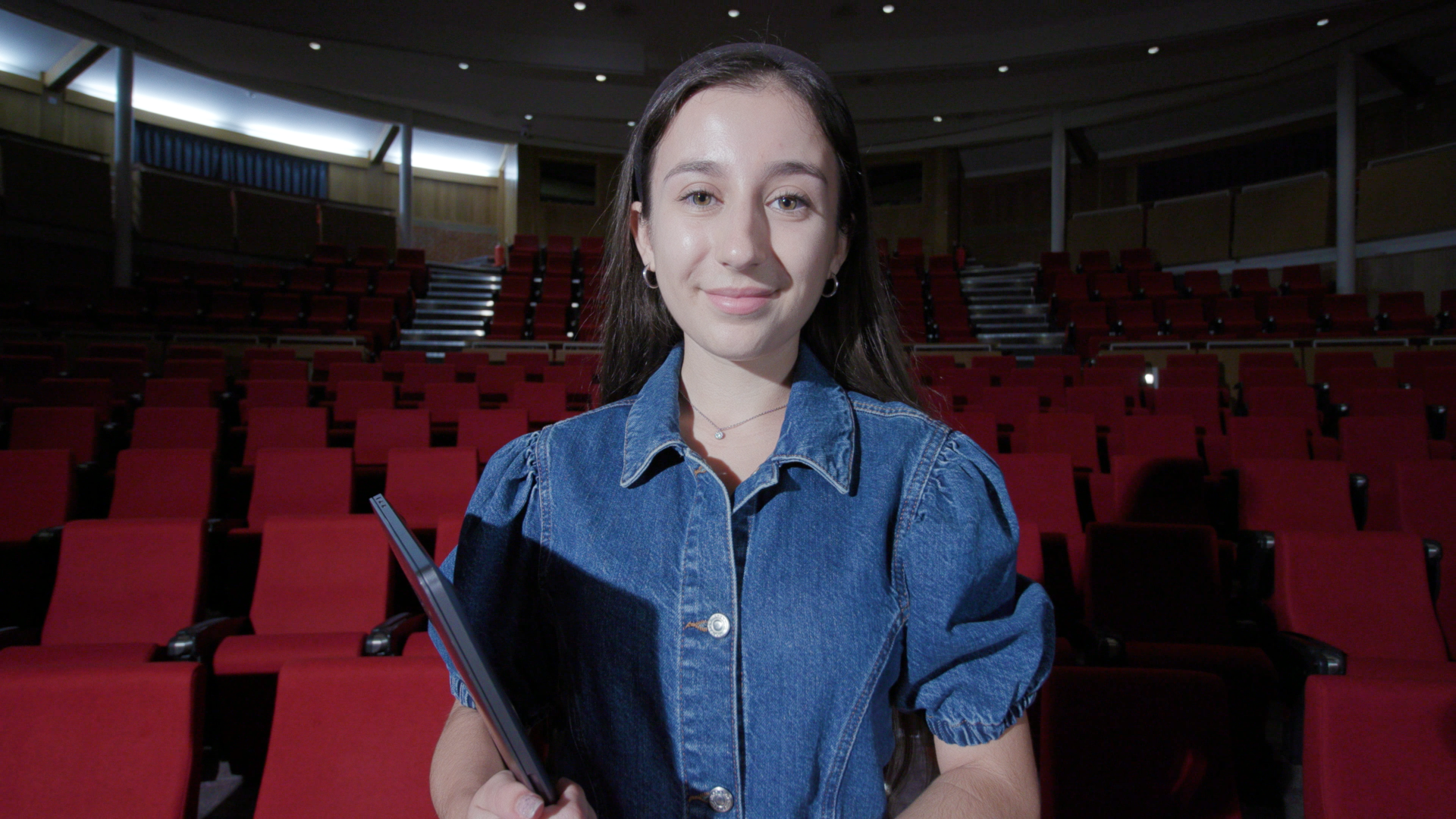 Picture of Leonie holding her laptop in a darkened empty theatre.