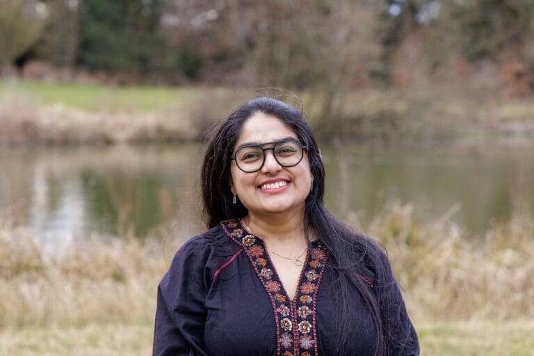 Image of Priyanka in front of a lake smiling at the camera.