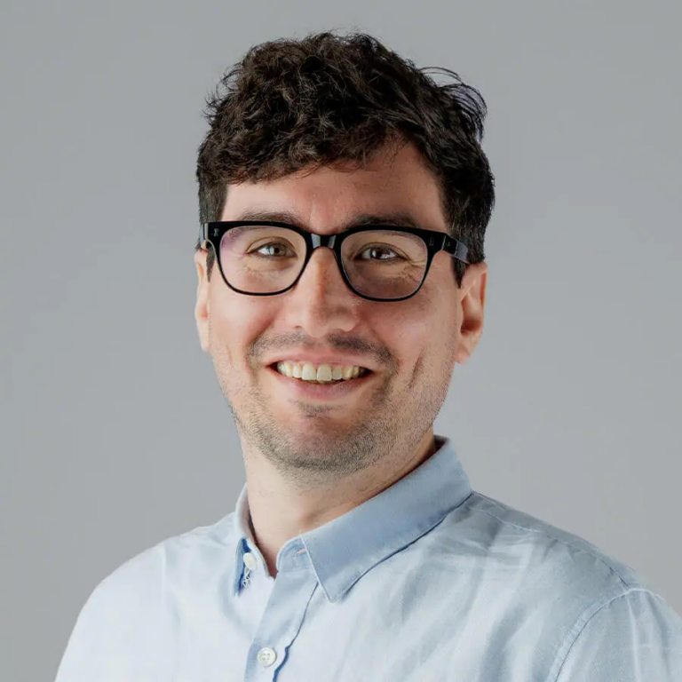 Image of Jonathan, a man wearing a light blue shirt, with glasses and dark brown hair, smiling.