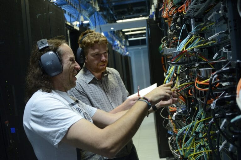 Two technicians fixing cables in a computer.