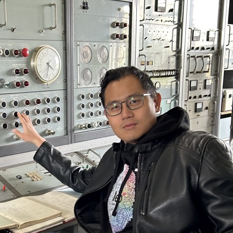 A headshot of Jimmy Lee posing comically in front of a complex control panel.